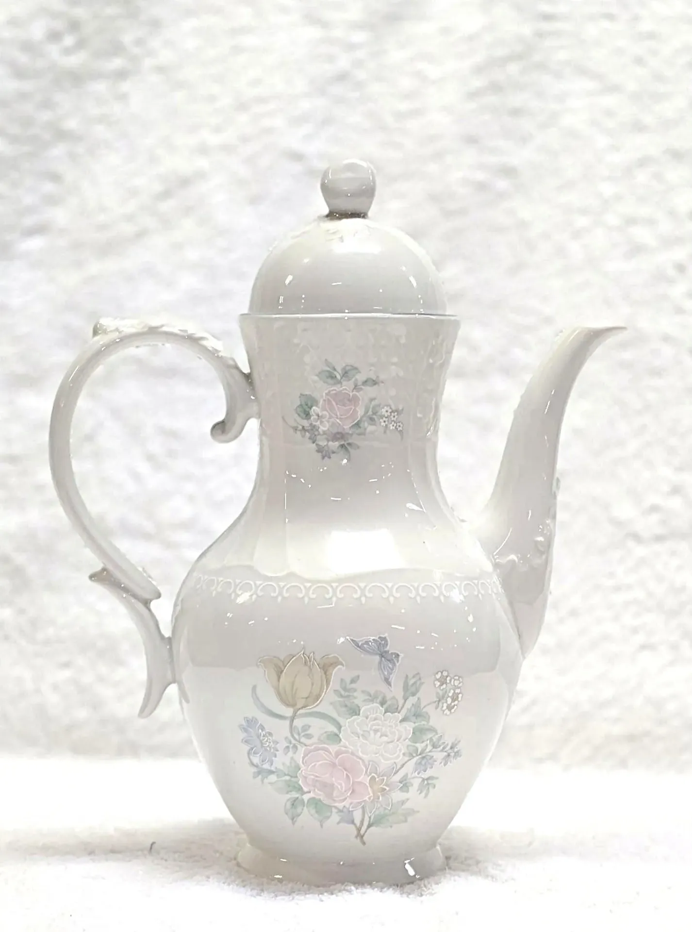 White ceramic coffee pot or teapot and lid with a delicate floral pattern.